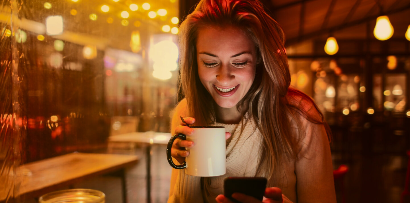A young woman enjoying a hot beverage is checking something on her phone.