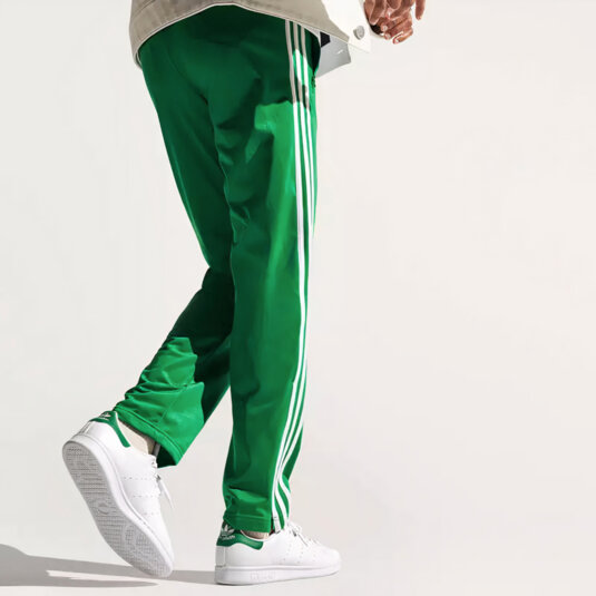 A person dressed in green Adidas sweatpants, wearing white Adidas sneakers.