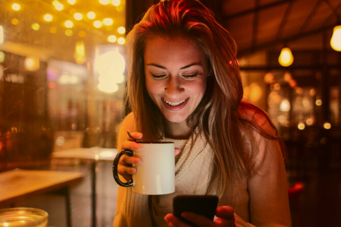 A young woman enjoying a hot beverage is checking something on her phone.