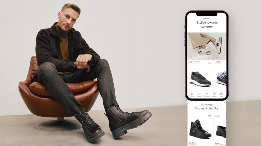 A man sitting on a chair, showing off his shoes. Next to him, there's a smartphone opened on the eobuwie app.
